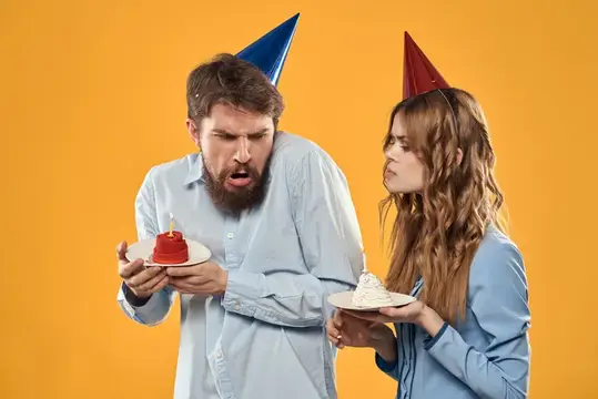 Удивлённый бородатый мужчина и девушка в праздничных колпаках с кексами