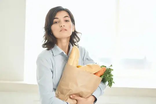 Молодая женщина с бумажным пакетом продуктов у окна