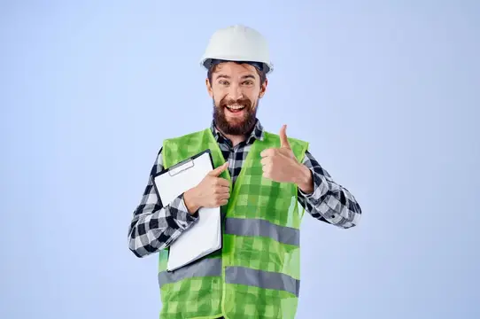 Улыбающийся бородатый строитель в каске и жилете показывает большой палец вверх