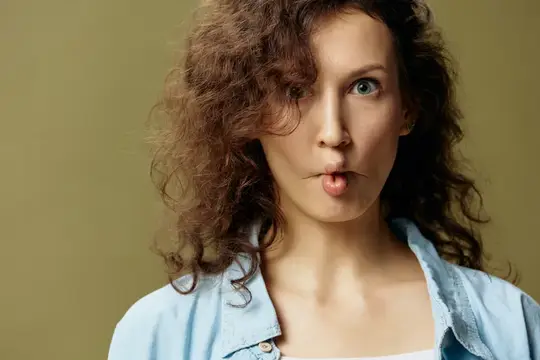 Кудрявая девушка с высунутым языком смотрит в камеру на оливковом фоне
