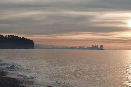 Спокойный закат над водой с силуэтом города и лесистого берега
