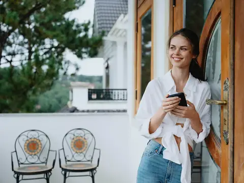 Женщина на балконе дома с телефоном, красивая улыбка в выходной день, красивый вид на природу в горах, образ жизни, отдых в отеле