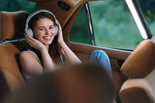 Улыбающаяся девушка в наушниках на заднем сиденье автомобиля