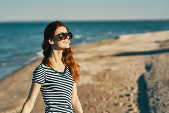 Красивая женщина в футболке и очках на пляже у моря в горах