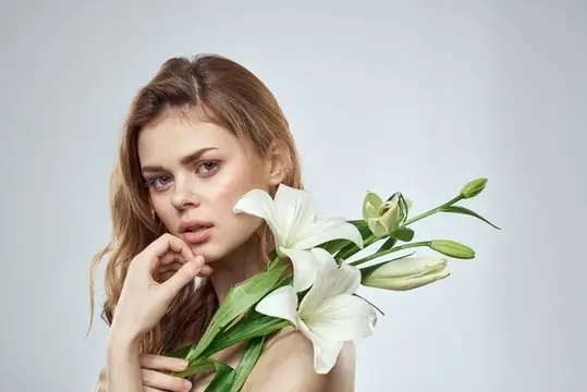 Молодая женщина с белыми лилиями у лица на сером фоне