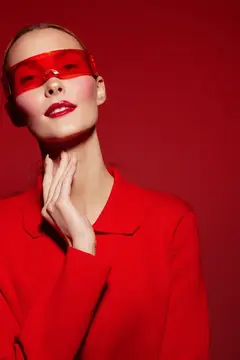 Модная женщина в красном свитере и красных полупрозрачных очках стоит на красном фоне