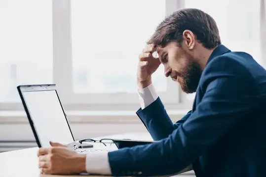 Уставший бородатый мужчина в костюме у ноутбука в офисе