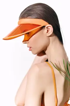Модная молодая женщина в ярком оранжевом козырьке и купальнике на фоне чистого белого фона