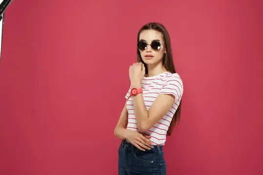 Молодая девушка в солнцезащитных очках позирует на розовом фоне