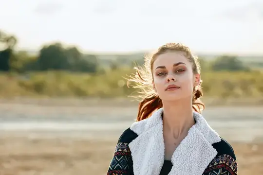 Молодая женщина с развевающимися волосами на фоне песчаного берега