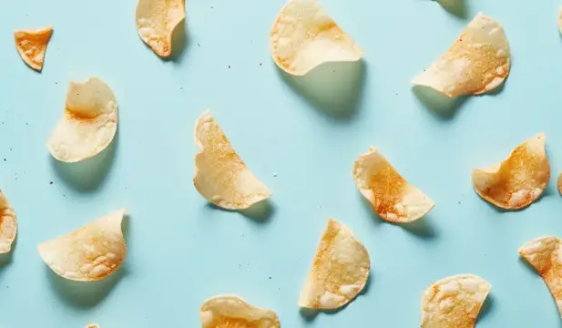 Ассорти из золотисто-коричневых картофельных чипсов, разложенных на мягкой голубой поверхности, демонстрирующее их хрустящую текстуру и неровные формы