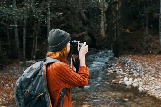 Женщина-туристка фотографирует природу: реку, лес и горы