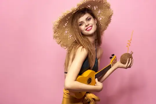 Улыбающаяся девушка в соломенной шляпе с укулеле и кокосом на розовом фоне