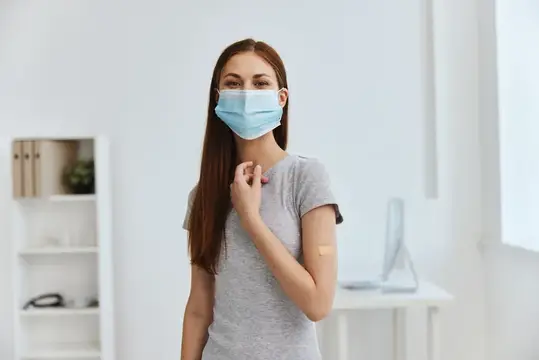 Молодая женщина в медицинской маске после вакцинации в светлом кабинете