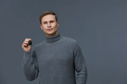 Молодой мужчина в сером свитере держит ключ от машины