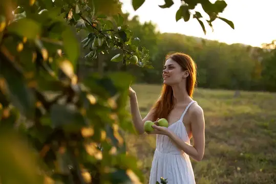Женщина в белом платье стоит рядом с яблоней на природе