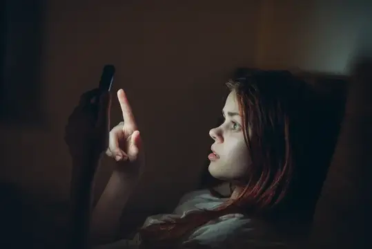 Девушка смотрит в телефон в темноте