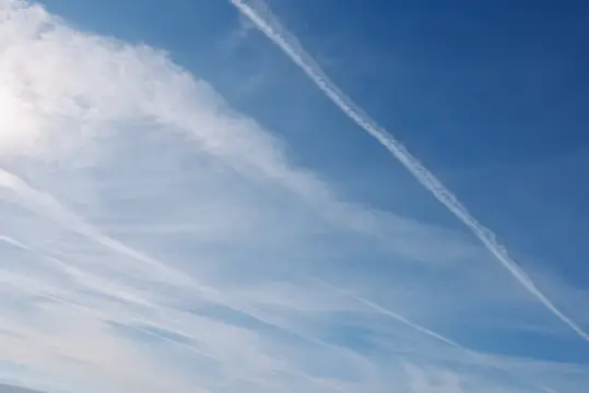 Белые инверсионные следы самолетов на фоне синего неба с облаками