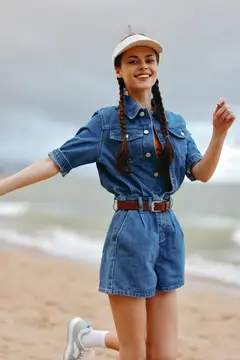 Улыбающаяся девушка с косичками в джинсовом комбинезоне на пляже