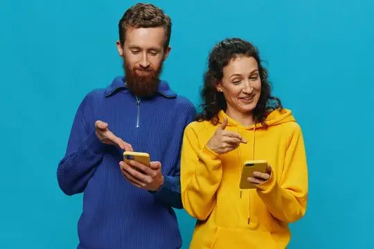 Бородатый мужчина и женщина в худи со смартфонами на синем фоне