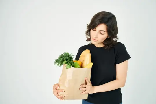 Молодая женщина с бумажным пакетом продуктов смотрит на свежую зелень