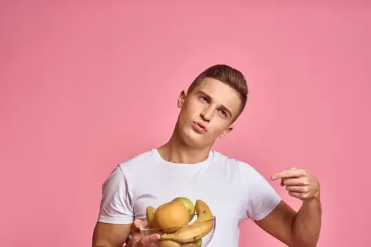 Мужчина с фруктами в руках на розовом фоне, здоровое питание, витамины, розовый фон, белая футболка, модель