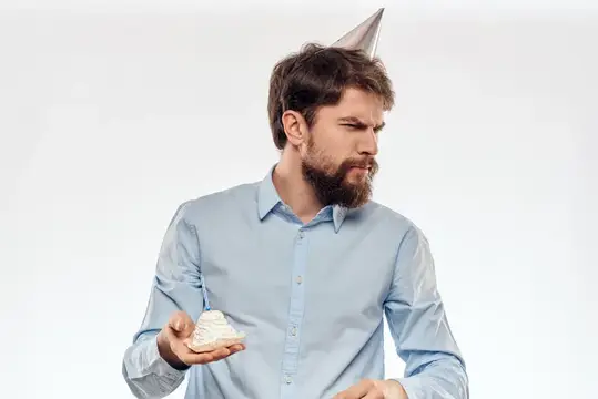 Задумчивый бородатый мужчина в праздничном колпаке с кусочком торта