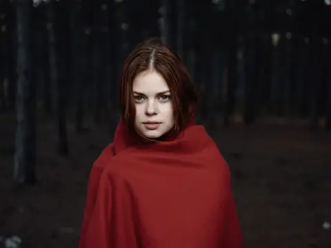 Рыжеволосая девушка в красном плаще в тёмном лесу