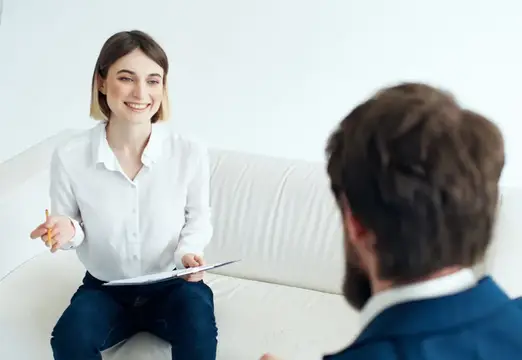 Улыбающаяся женщина с блокнотом беседует с мужчиной на диване