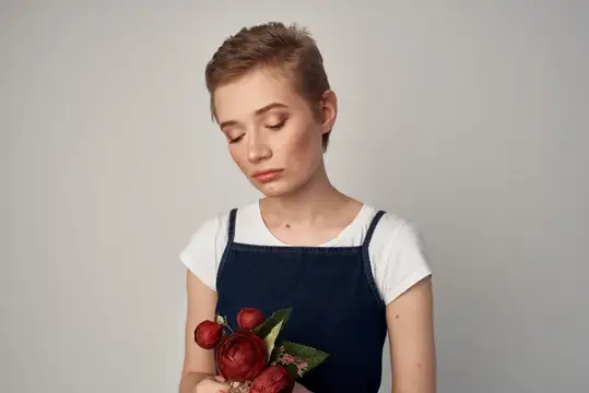 Молодая женщина с короткой стрижкой держит красные розы и грустно смотрит вниз