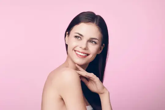 Улыбающаяся молодая женщина с белым полотенцем на розовом фоне