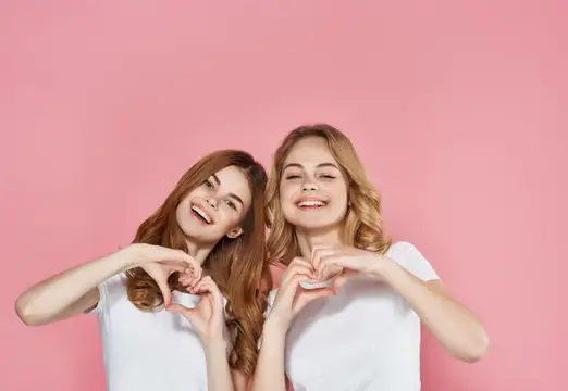 Женщины в белых футболках стоят рядом на розовом фоне, демонстрируя эмоции и дружбу