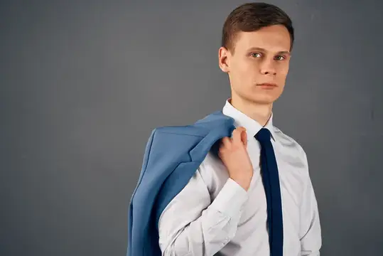 Молодой человек в белой рубашке с галстуком держит пиджак на плече