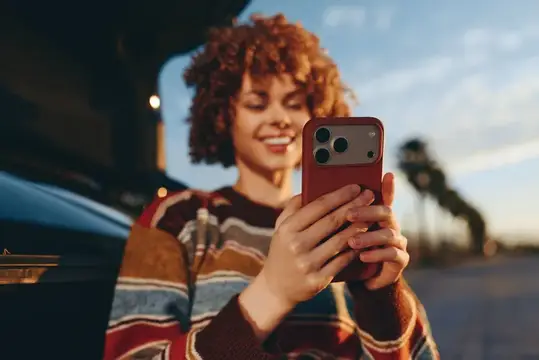 Улыбающаяся кудрявая девушка смотрит в смартфон на закате