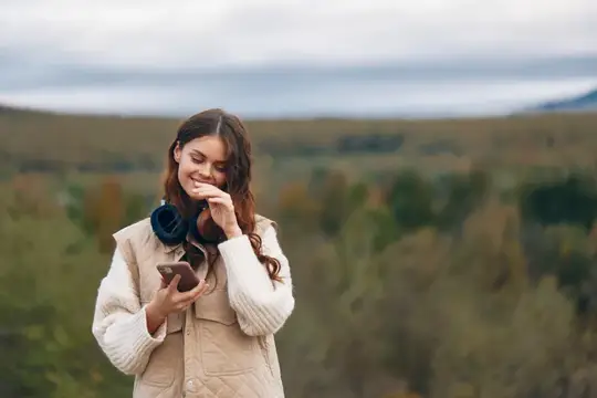 Улыбающаяся девушка с телефоном на фоне осенних холмов