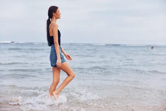 Молодая женщина босиком бежит по кромке воды на пляже