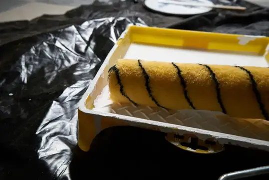 Жёлтый малярный валик с чёрными полосами в лотке на чёрной плёнке