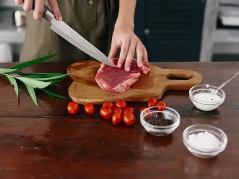 Женщина с ножом в руке нарезает мясо стейка для жарки на кухне