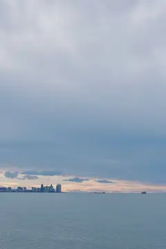 Спокойное море и силуэт далекого города вдоль широкого горизонта, нежные облака в сумерках, безмятежная водная сцена, идеально подходящая для пейзажных изображений или изображений в стиле открыток