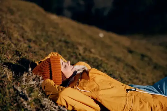 Женщина красиво лежит на холме, улыбается, обнажая зубы, в горах осенью, в жёлтом дождевике и джинсах, счастливая, на закате, в походе в горы, на снегу, образ жизни, полный свободы