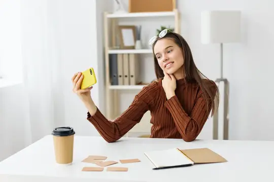 Улыбающаяся девушка с телефоном за столом в светлом офисе