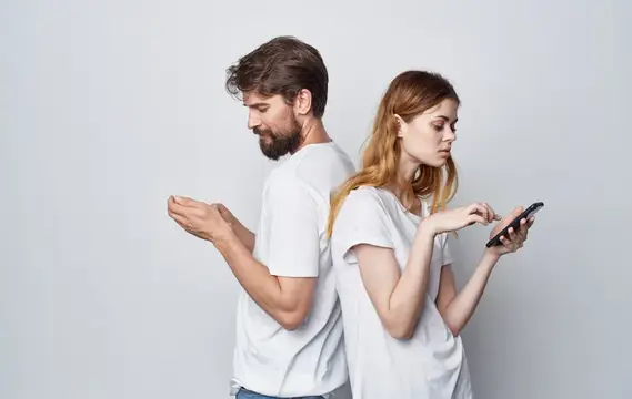Мужчина и рыжеволосая женщина стоят спиной к спине со смартфонами