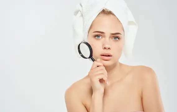 Женщина с белым полотенцем на голове касается руками лица на светлом фоне
