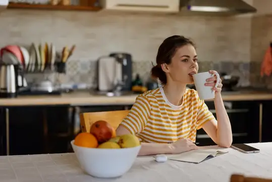 Молодая женщина пьёт кофе за столом на светлой кухне