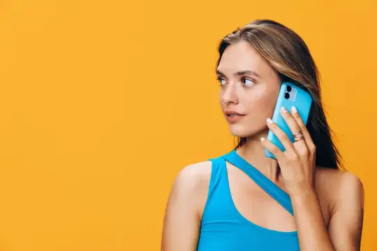 Молодая женщина с голубым смартфоном у уха на жёлтом фоне