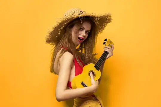 Улыбающаяся девушка в соломенной шляпе играет на жёлтой укулеле на оранжевом фоне