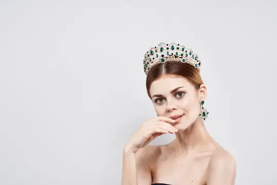 Молодая женщина в роскошной короне с изумрудами на светлом фоне