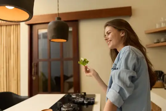 Улыбающаяся девушка держит веточку зелени на кухне