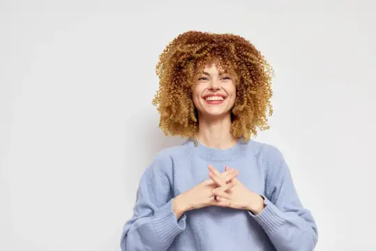 Улыбающаяся кудрявая девушка в голубом свитере на белом фоне