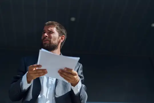 Бородатый мужчина в костюме эмоционально читает документы